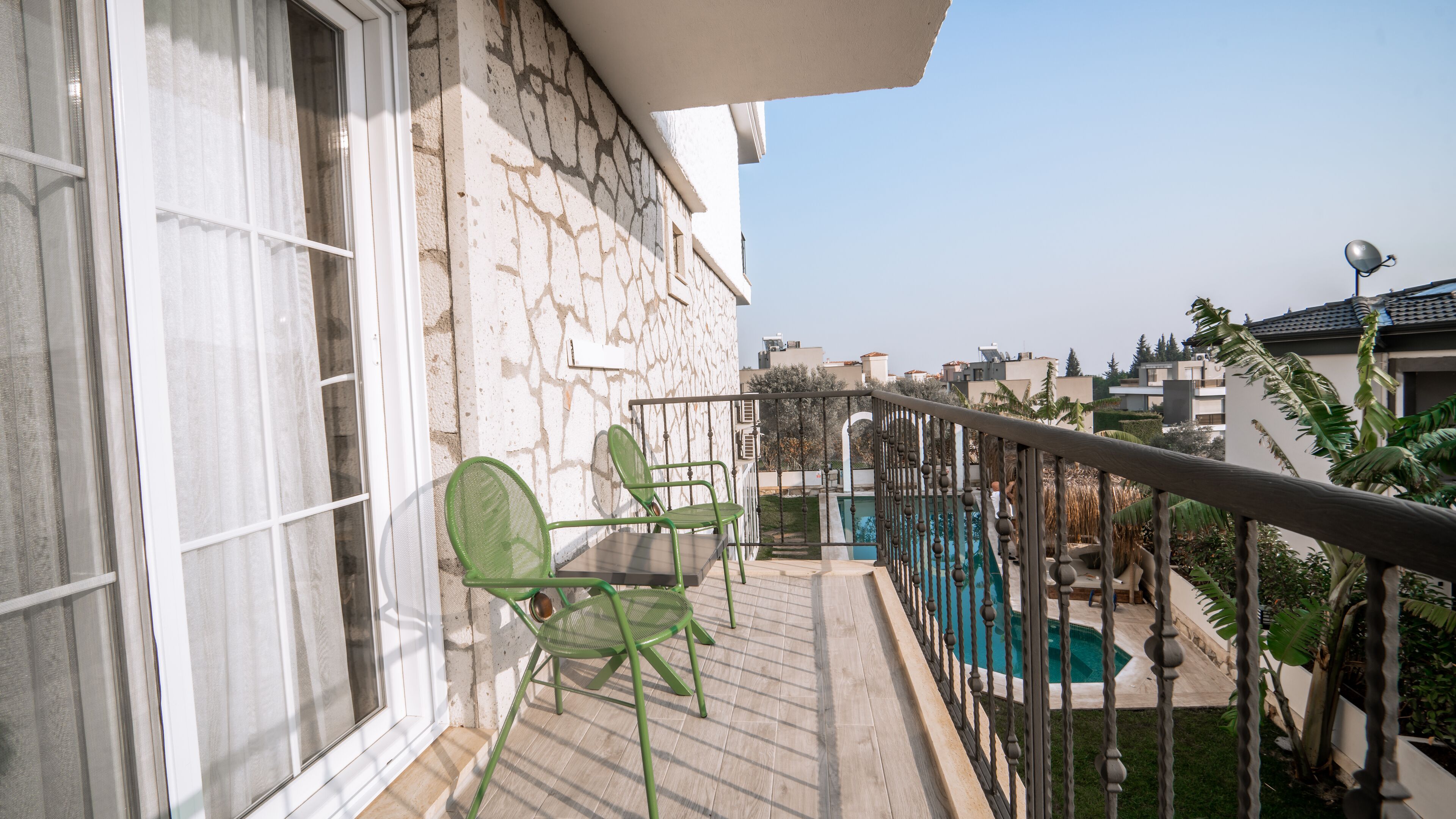 A balcony with a pool, stone wall, and two green chairs.