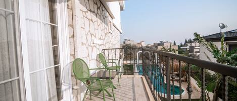 A balcony with a pool, stone wall, and two green chairs.