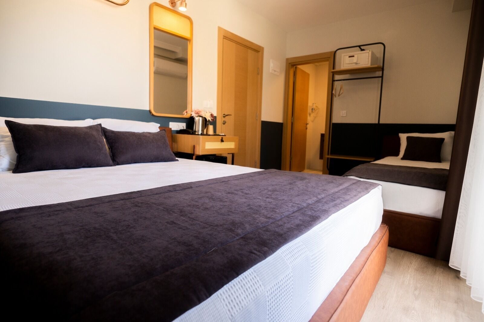 Ein Hotelzimmer mit einem großen Bett, einem Einzelbett, einem Schreibtisch mit Stuhl, einem Spiegel und einem Kleiderschrank.