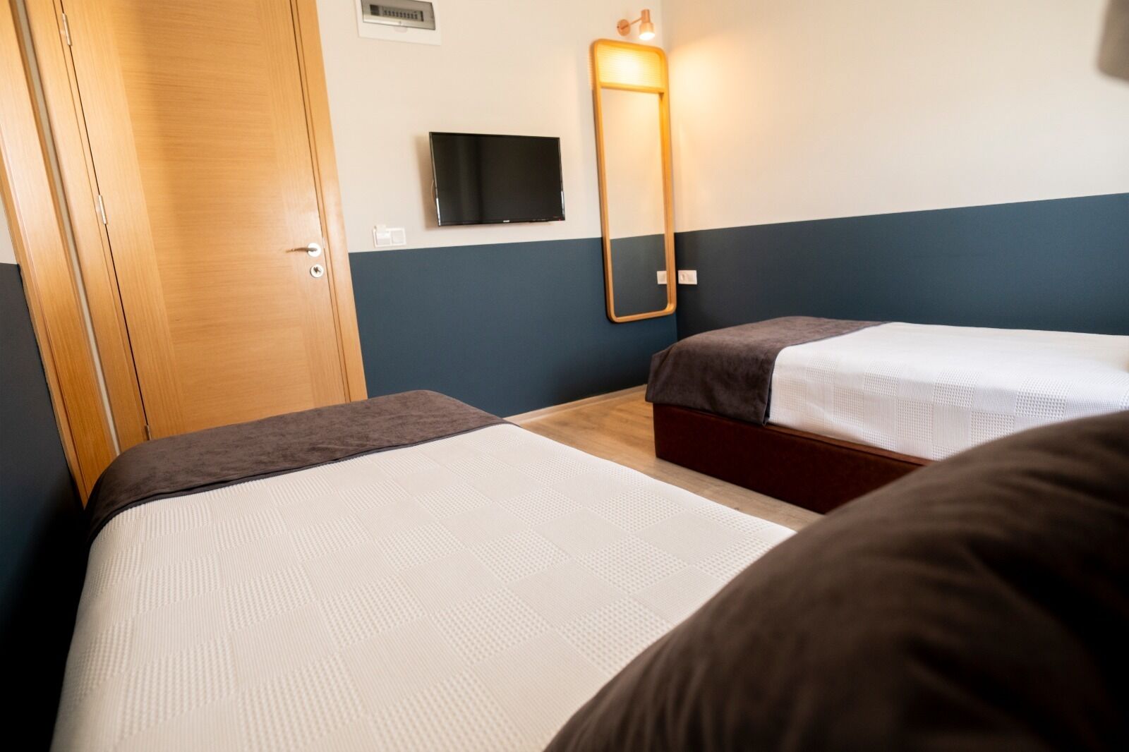 Une chambre d’hôtel avec deux lits, une télévision, un miroir et une armoire en bois.