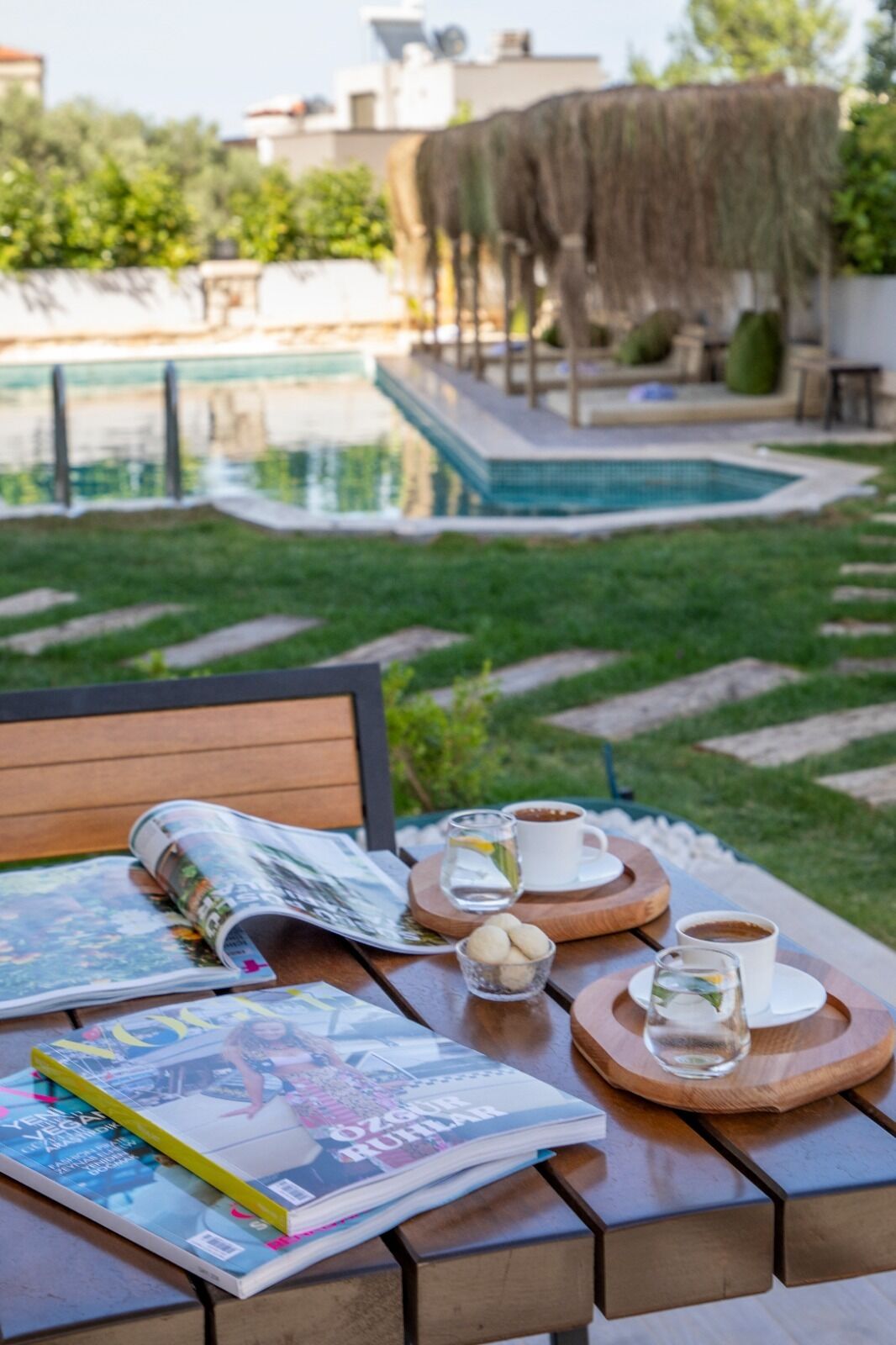 Une table en bois avec des magazines, une tasse de café et un verre d’eau.