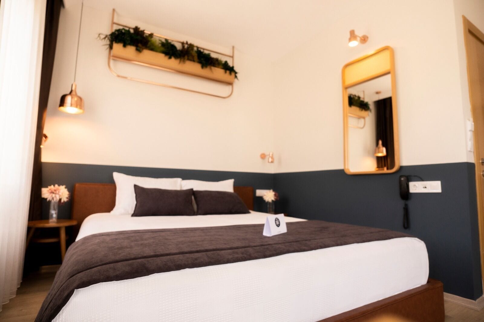 A hotel room with a bed, bedside tables, a mirror, and a wall-mounted plant.