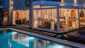 Un hotel de varios pisos con piscina, fachada de piedra, balcones y zonas de estar al aire libre.