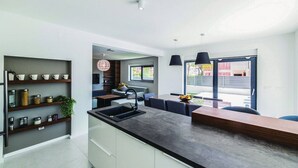 A modern kitchen with a central island, built-in shelves, and a dining area with a view. - Luxury Dream House in Kaštel Novi (Kaštel Novi)