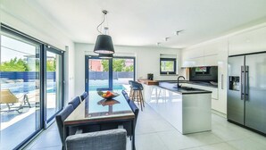 A modern kitchen with a central island, stainless steel appliances, and a dining area with a glass table and chairs. - Luxury Dream House in Kaštel Novi (Kaštel Novi)
