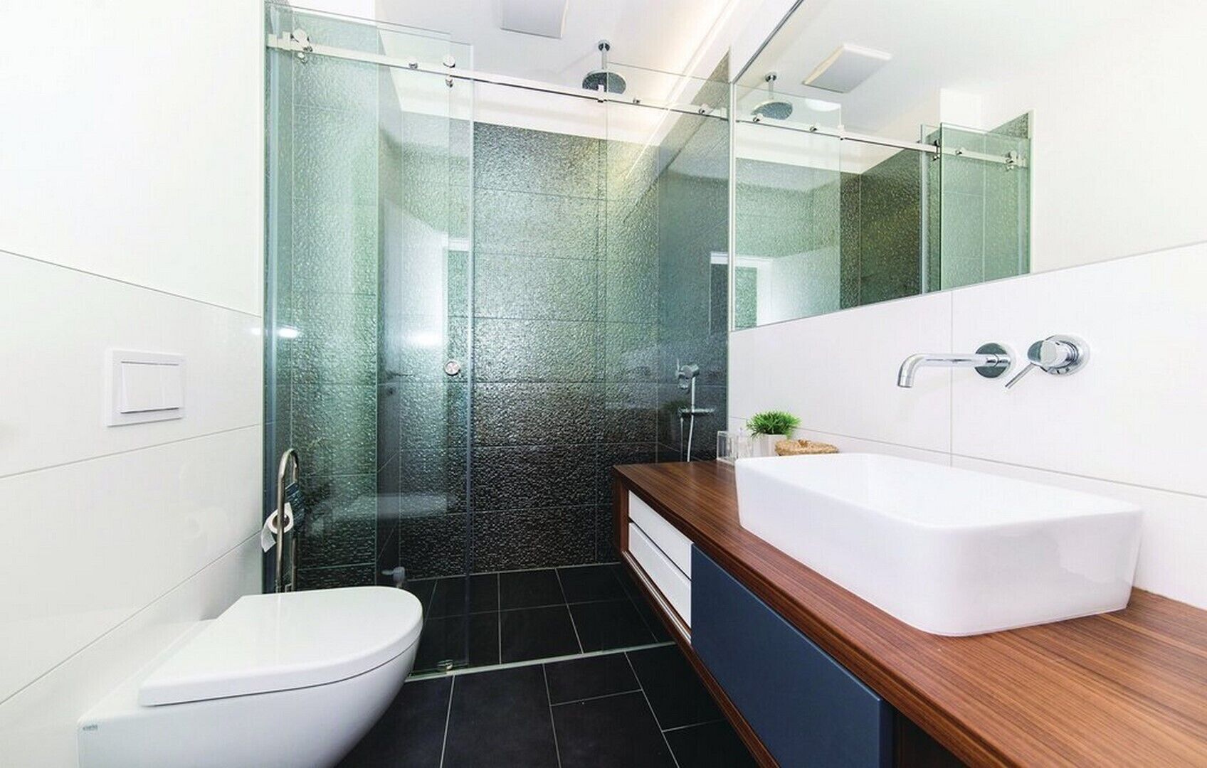 Een moderne badkamer met een glazen douchecabine, een wit toilet en een houten wastafelmeubel met een witte wastafel.