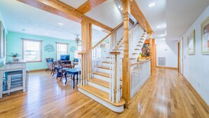 A spacious living area with a wooden staircase, a dining area, and a kitchen. - Glad Tidings - KDH MP 7.5, 320 Yds to Beach, Elevator, Indoor Pool, Hot Tub, Pets OK, Flex Stays (Kill Devil Hills)