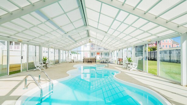 A covered swimming pool with clear glass walls, a central seating area, and potted plants. - Glad Tidings - KDH MP 7.5, 320 Yds to Beach, Elevator, Indoor Pool, Hot Tub, Pets OK, Flex Stays (Kill Devil Hills)