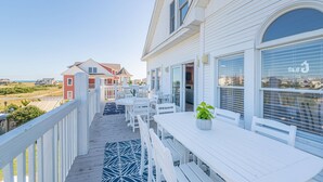 A covered outdoor area with white wooden furniture, including tables and chairs, and a potted plant. - Glad Tidings - KDH MP 7.5, 320 Yds to Beach, Elevator, Indoor Pool, Hot Tub, Pets OK, Flex Stays (Kill Devil Hills)