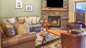 A living room with a stone fireplace, leather sofas, and a flat-screen TV mounted above it.