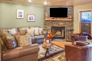 A living room with a stone fireplace, leather sofa, and a flat-screen TV mounted above it.