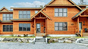 A two-story wooden house with a front porch, large windows, and a stone pathway leading to the entrance.