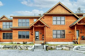 A multi-story wooden cabin with a porch, large windows, and a stone foundation.