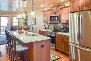A kitchen with wooden cabinets, stainless steel appliances, a granite countertop, and a central island with bar stools.