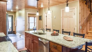 A kitchen with granite countertops, wooden cabinets, and a central island with a sink. There are two pendant lights above the island.