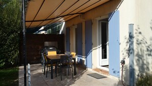An outdoor patio with a table and chairs, a barbecue grill, and a covered area with a roof.