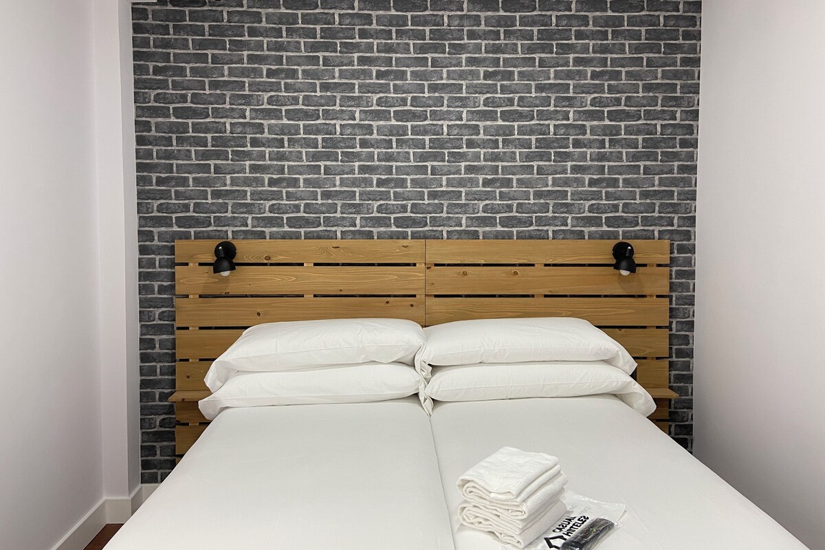 Una cama con cabecera de madera frente a una pared de ladrillo.