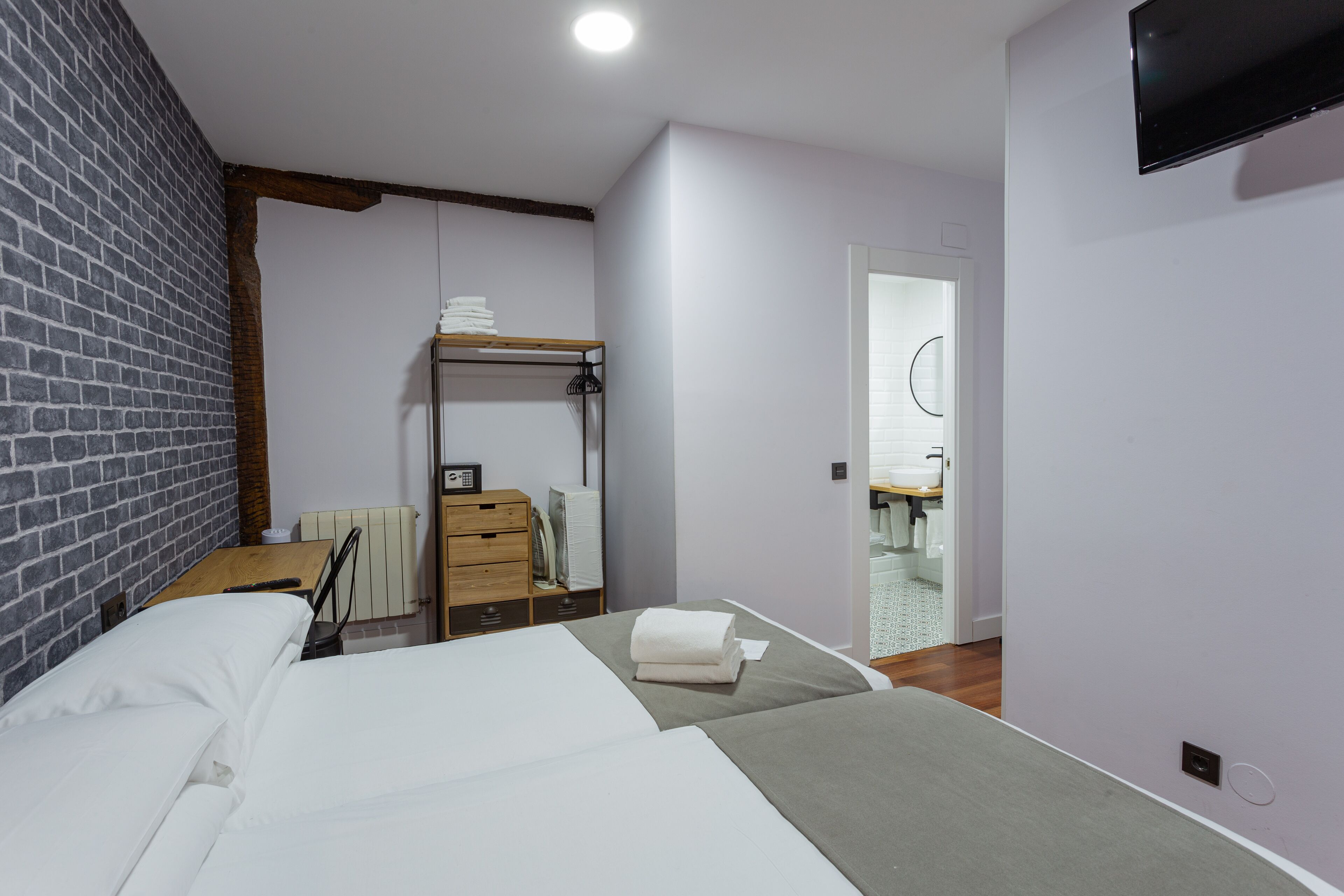 Habitación de hotel con cama, escritorio de madera, espejo y televisor en la pared.