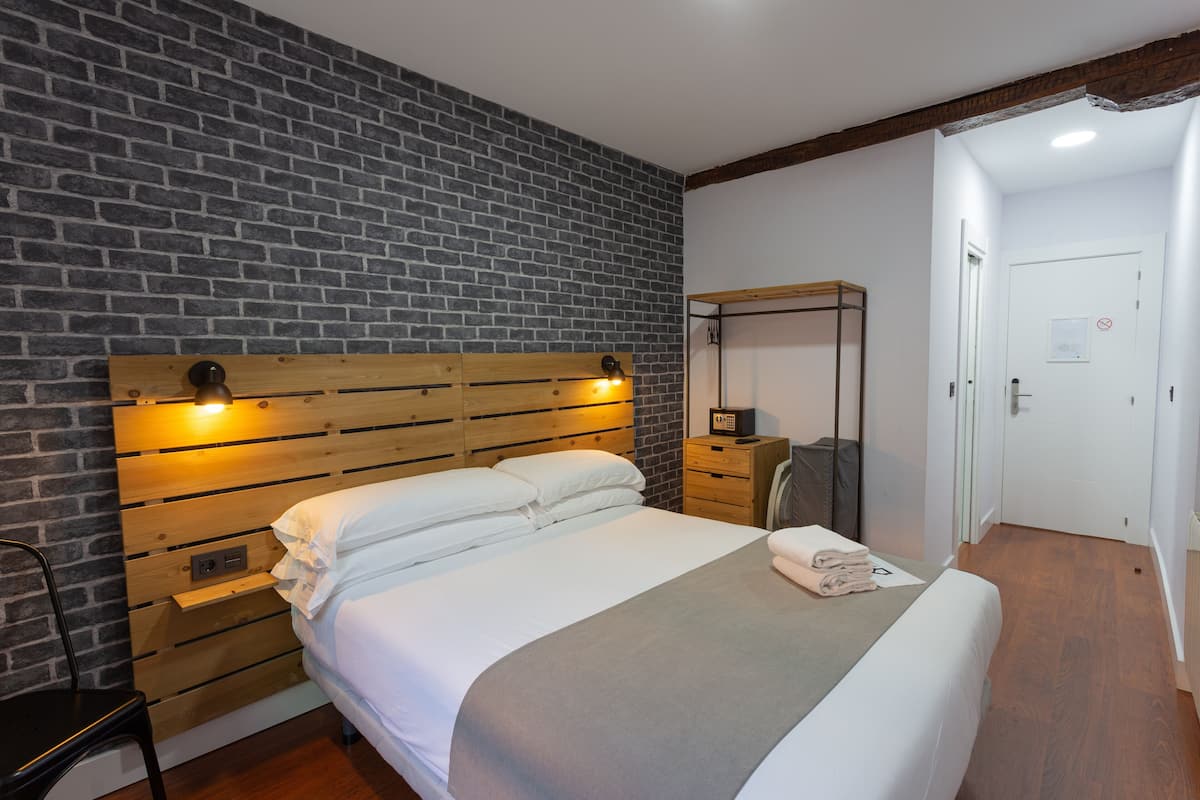 Hotellihuone, jossa on tiilikuviollinen seinä, puinen sängynpääty, jossa on sisäänrakennettu valaistus, valkoisilla lakanoiden peitetty sänky, yöpöytä lampun kanssa ja ovi, jossa on kyltti, jossa lukee ”sisäänpääsy kielletty”.