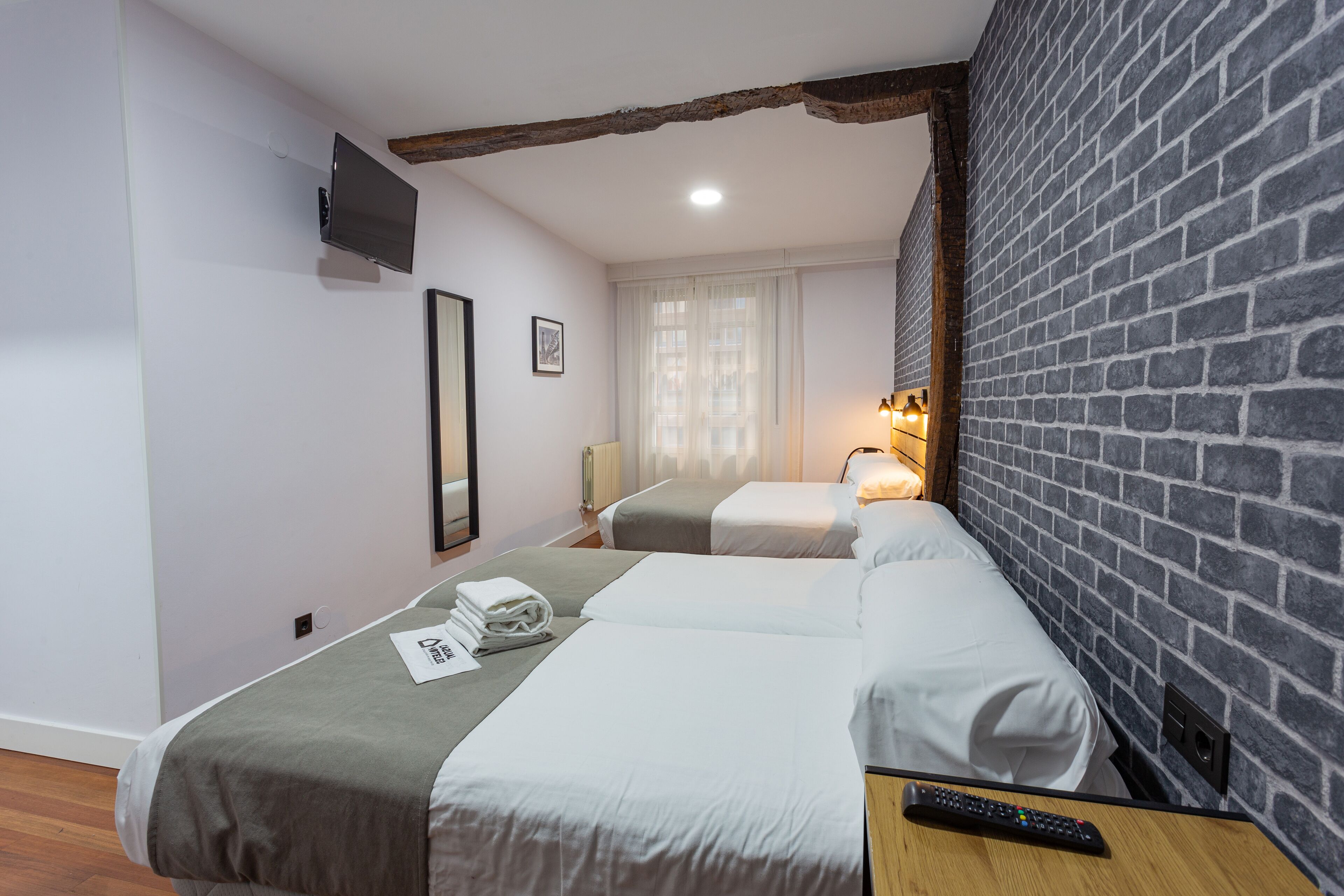 Ein Hotelzimmer mit zwei Betten, einem an der Wand befestigten Fernseher und einer Ziegelwand.