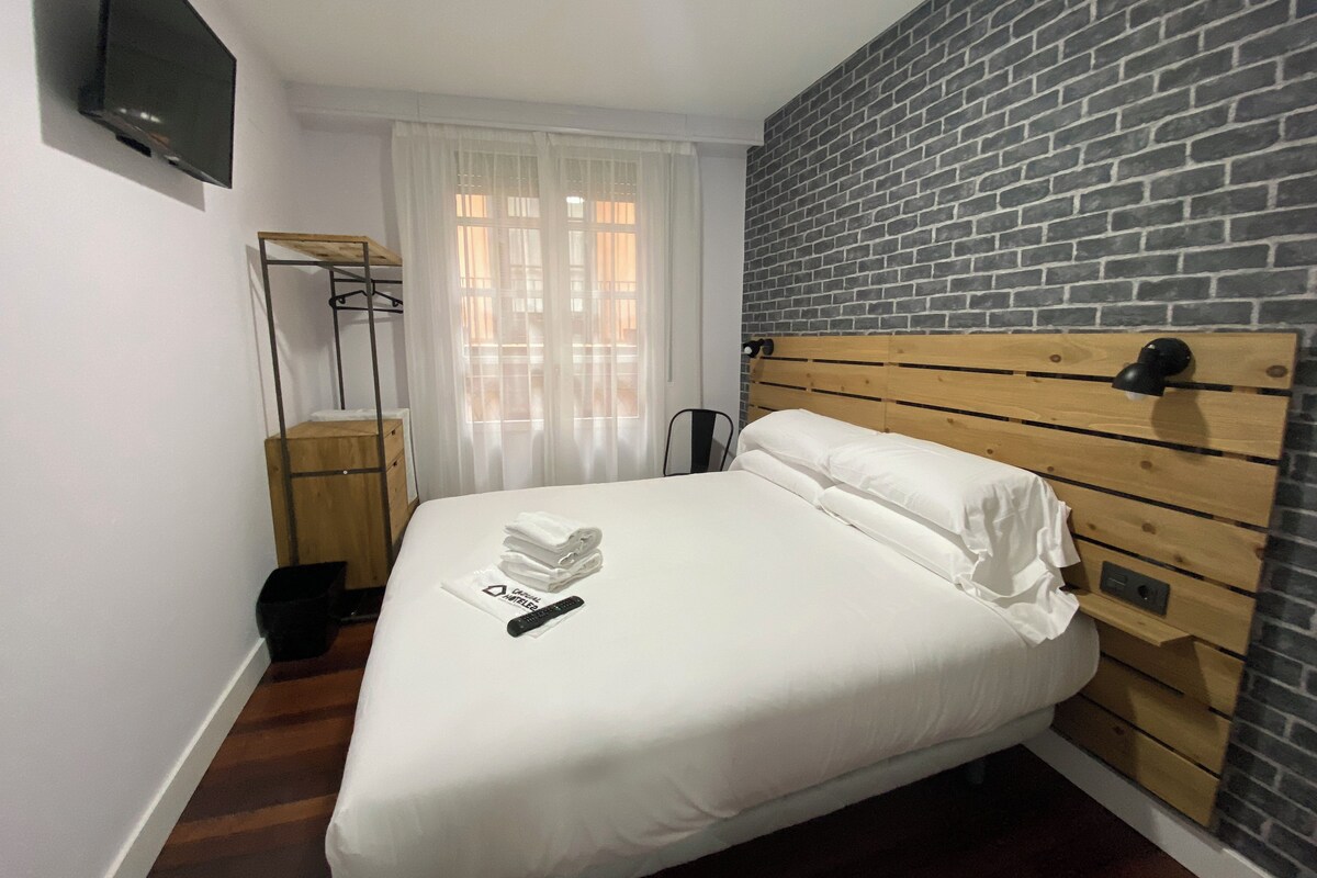 Una cama bien hecha con sábanas blancas, cabecera de madera y un control remoto sobre la cama.