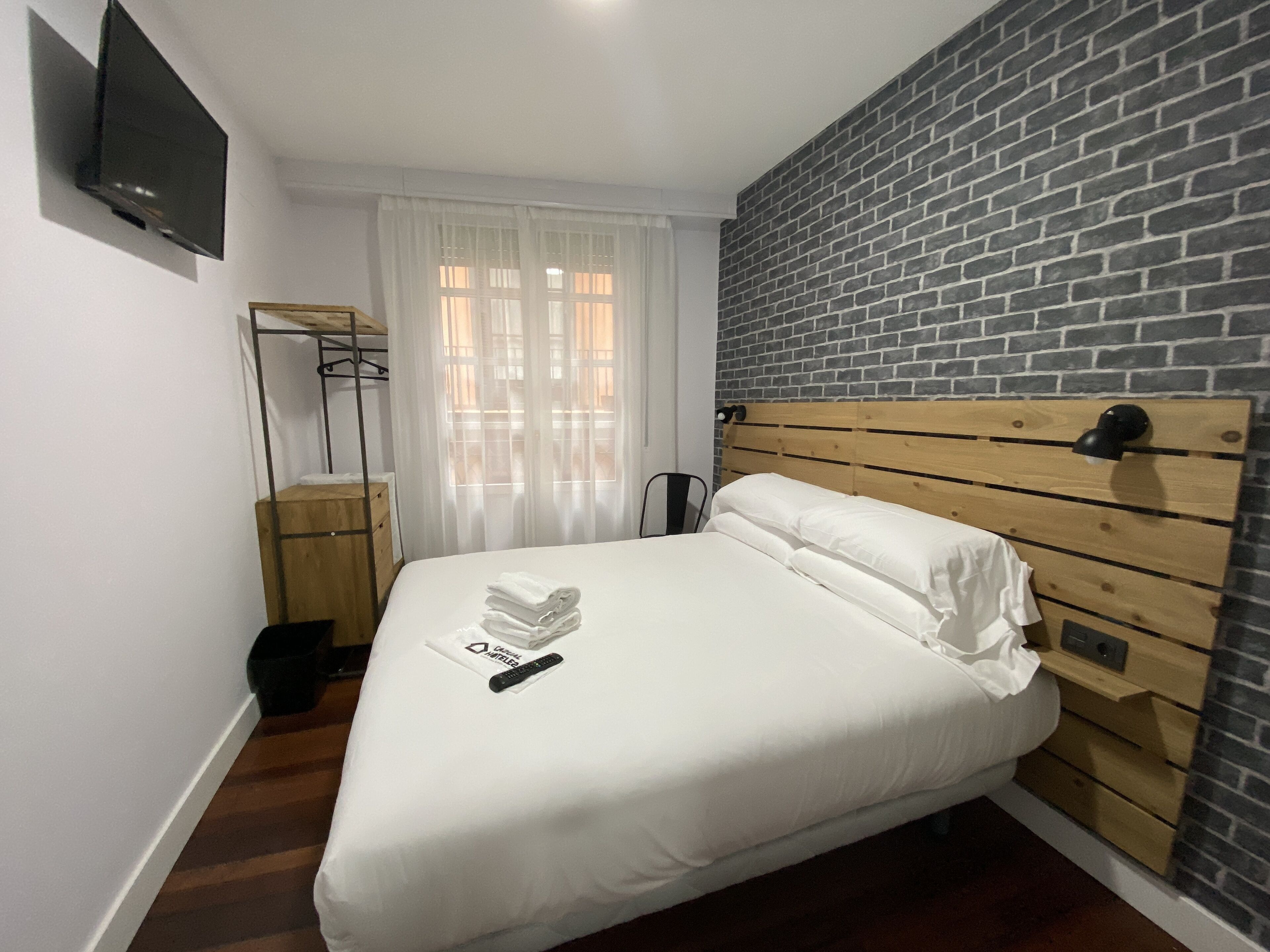 A neatly made bed with white linens, a wooden headboard, and a remote control on the bed.