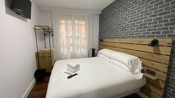 Una cama bien tendida con sábanas blancas, cabecera de madera y un control remoto sobre la cama.