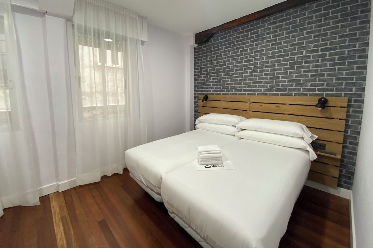 A neatly made bed with white linens, a wooden headboard, and a brick-patterned wall behind it.
