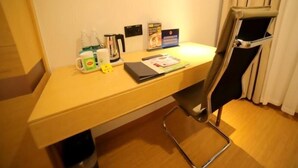 Ett hotellrum med ett skrivbord i trä, en stol, en kaffebryggare, en vattenkokare, en näsdukask och en liten papperskorg.