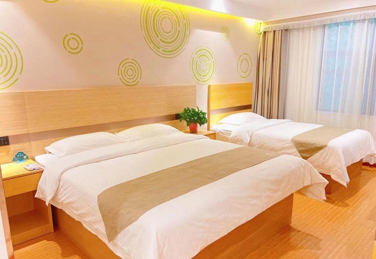 A hotel room with two beds, a nightstand, a potted plant, and a window with curtains.