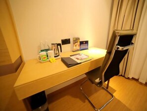 Ein Hotelzimmer mit einem Holztisch, einem Stuhl, einer Kaffeemaschine, einem Wasserkocher, einer Taschentuchbox und einer kleinen Mülltonne.