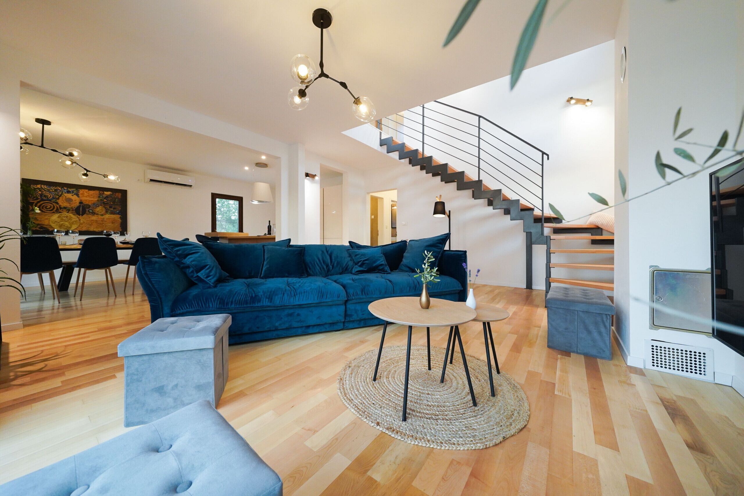 Een moderne woonkamer met een blauwe bank, een ronde salontafel en een trap.