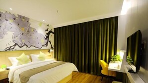 A hotel room with a bed, a desk, a chair, a television, and a wall with a floral design. - Vatica Huanggang Luotian County City Square Hotel (Huanggang)