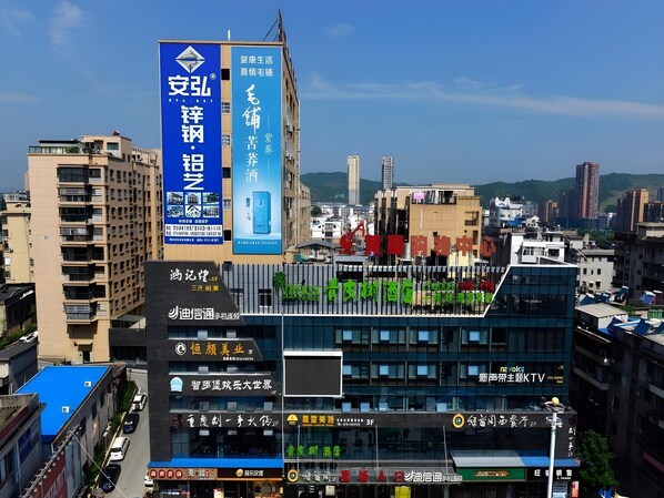 A cityscape with a prominent building featuring a large blue sign with white text, a modern glass facade, and a rooftop garden.