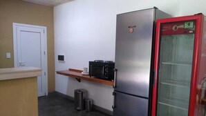 Een praktische keuken met een koelkast, magnetron en een rode drankdispenser.