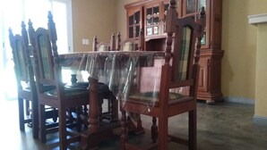 Een eethoek met houten stoelen en een tafel, een houten kast en een raam met jaloezieën.