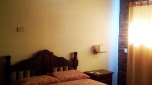 Een kamer met weinig licht, een houten bed, een nachtkastje en een raam met gordijnen.