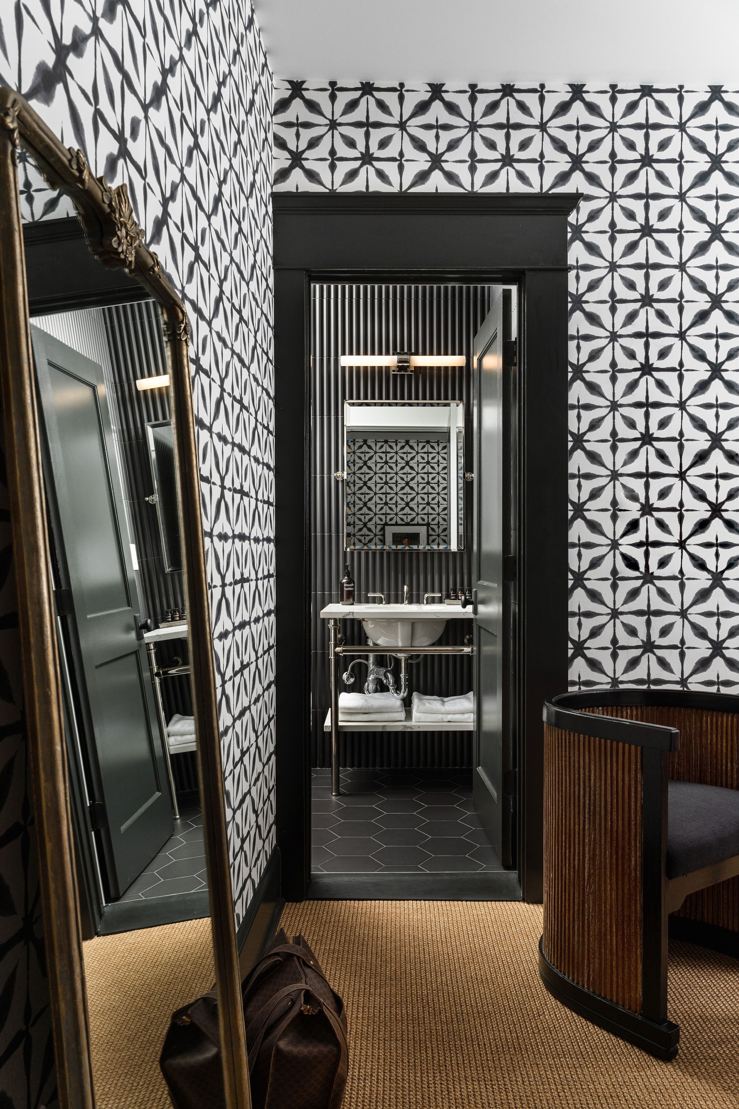 A modern bathroom with a geometric patterned wall, a large mirror, and a wooden vanity.