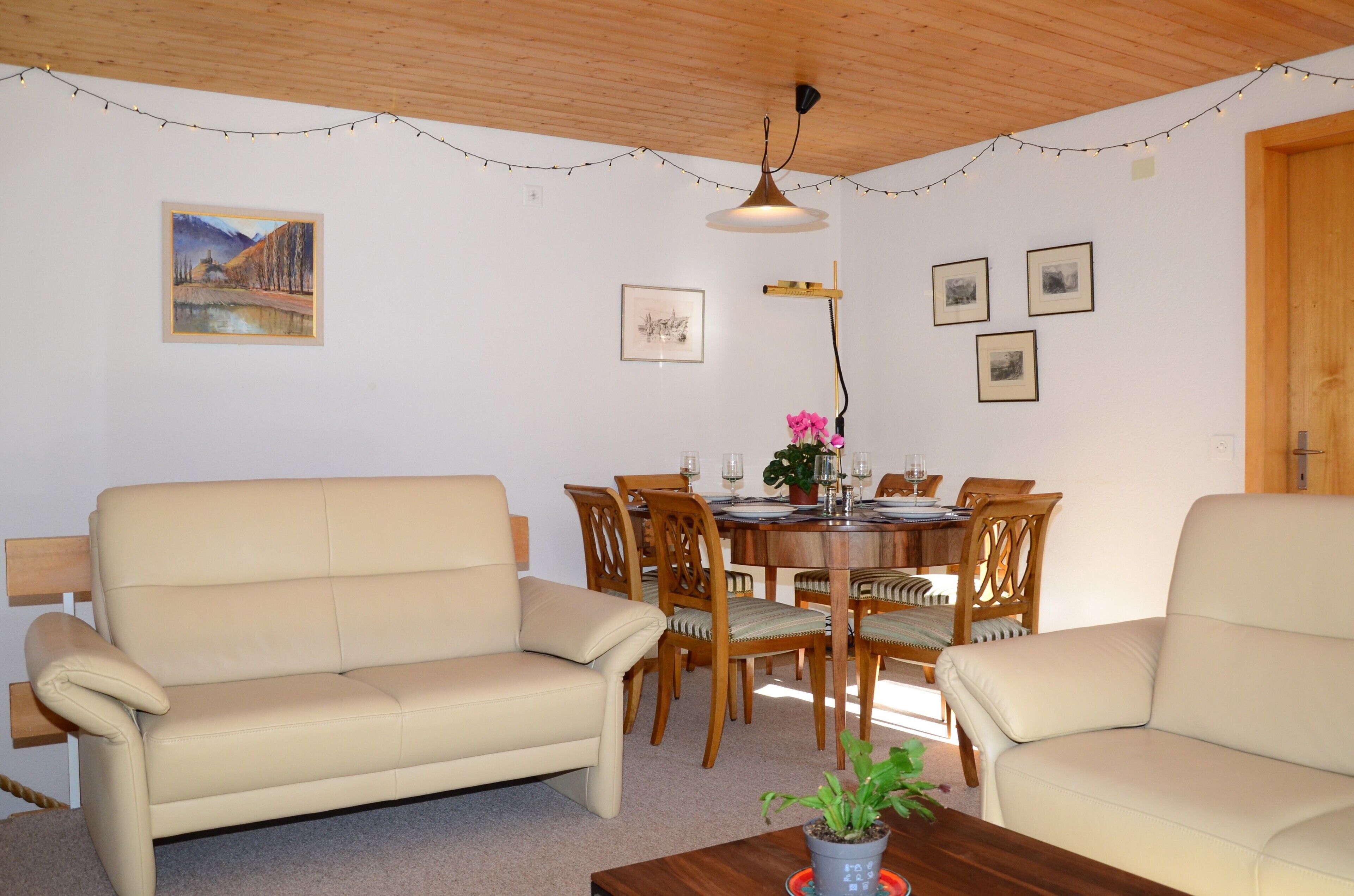 A cozy living room with two beige sofas, a wooden dining table with chairs, and a ceiling light fixture.