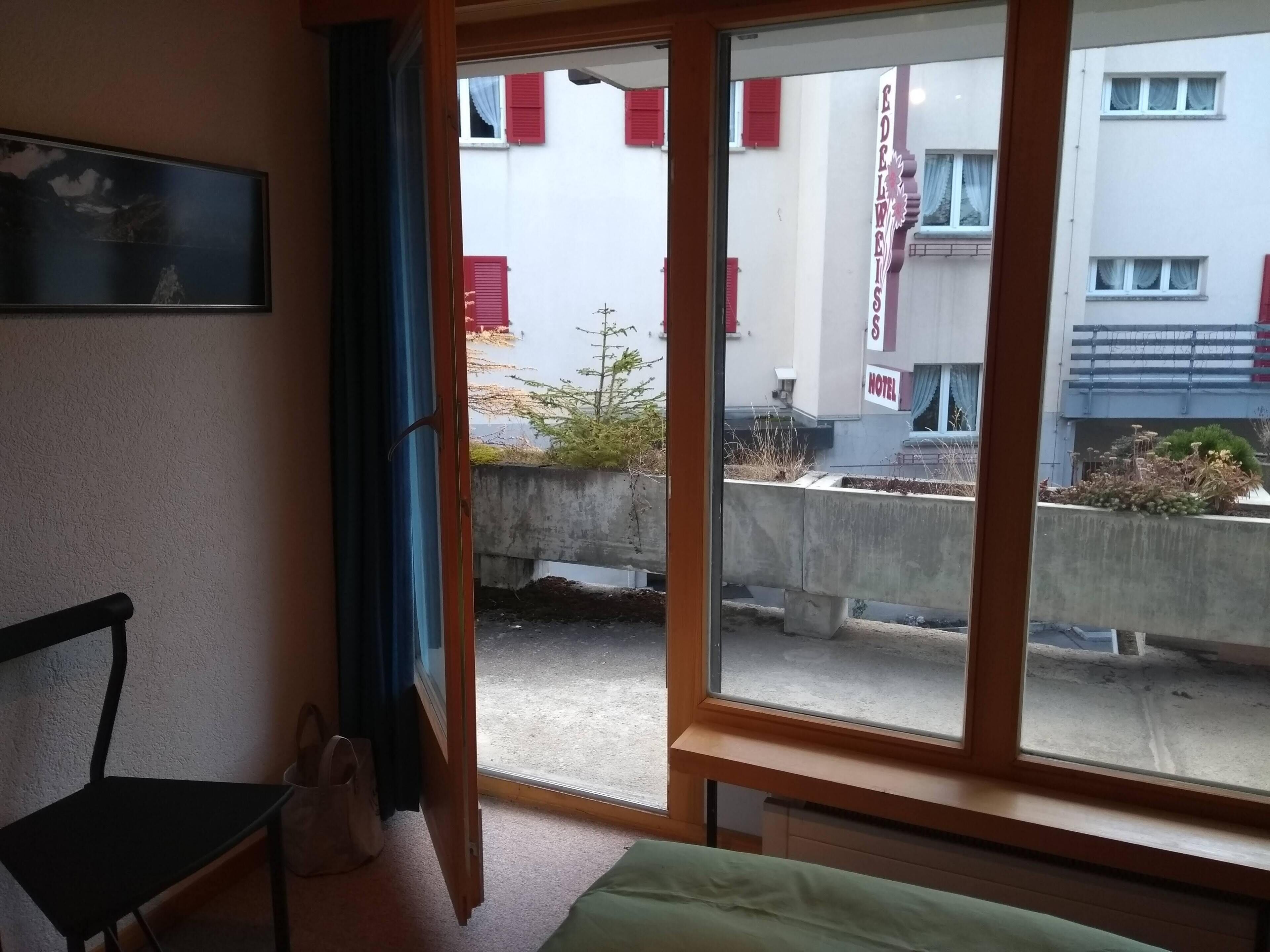 A hotel room with a large window, a bed, a chair, and a small table.