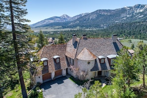 A large, stone house with a tiled roof, surrounded by trees and mountains.