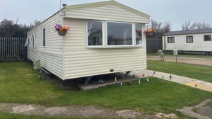A single-story mobile home with a window, a small porch area, and a visible water spigot.