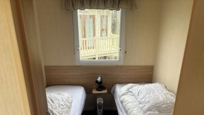 A compact room with two single beds, a small table with a lamp, a window with a view of a balcony, and a radiator.