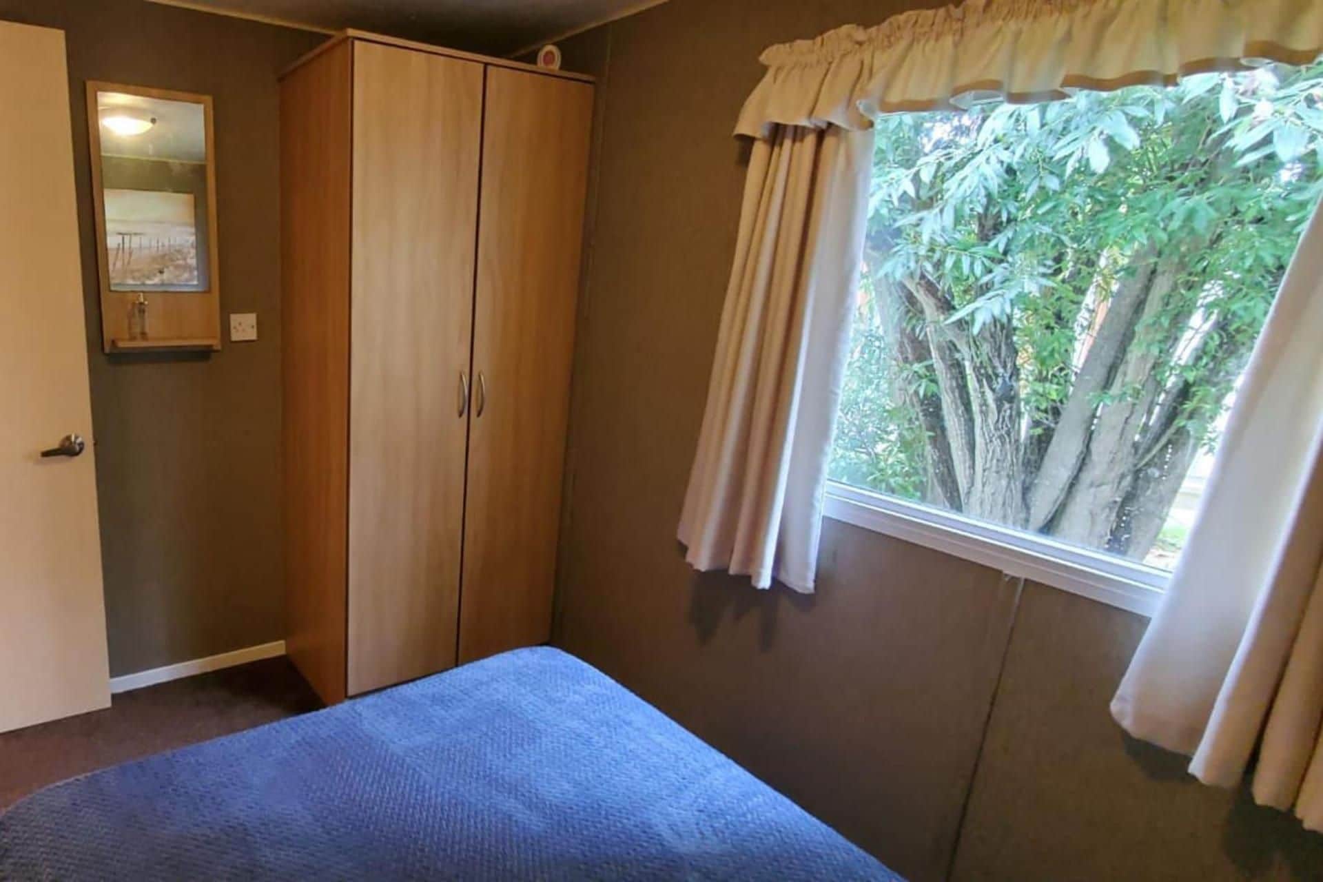 A bedroom with a bed, a wardrobe, a window with curtains, and a mirror.