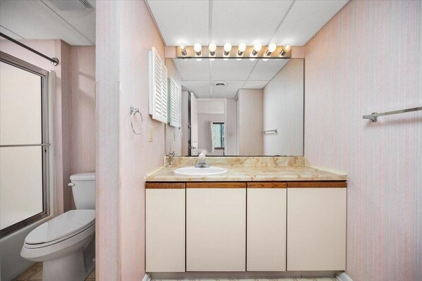 A bathroom with a white toilet, a sink with a marble countertop, and a mirror above the sink. - Rainbow - Beautiful Oceanfront 3 Bedroom Condo with Outdoor Pool! (Ocean City)