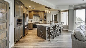A spacious kitchen with wooden cabinets, a central island, and a dining area with chairs. - 2112 SeaCrest -Stunning Villa offers Lowcountry luxury living! (Hilton Head Island)