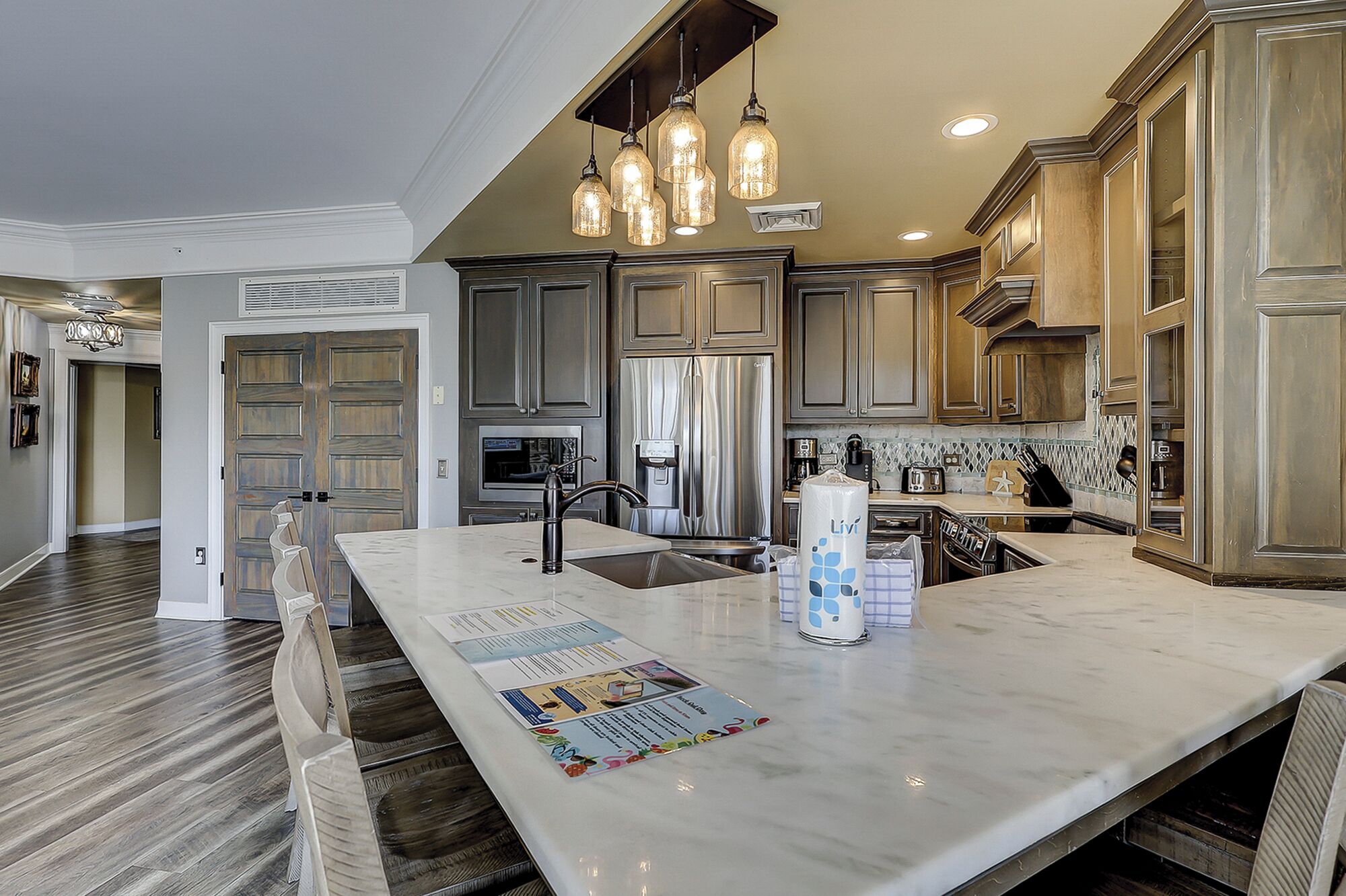 A kitchen with a marble island, stainless steel appliances, and pendant lighting.