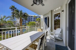 A balcony with a table and chairs, a ceiling fan, and a view of a building with balconies and palm trees.