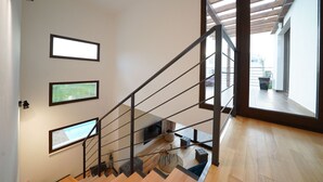 Una escalera moderna con peldaños de madera y barandillas de metal, que conduce a un balcón con vistas al exterior.