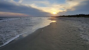 Ein Strand mit blauem Himmel und der untergehenden Sonne am Horizont.